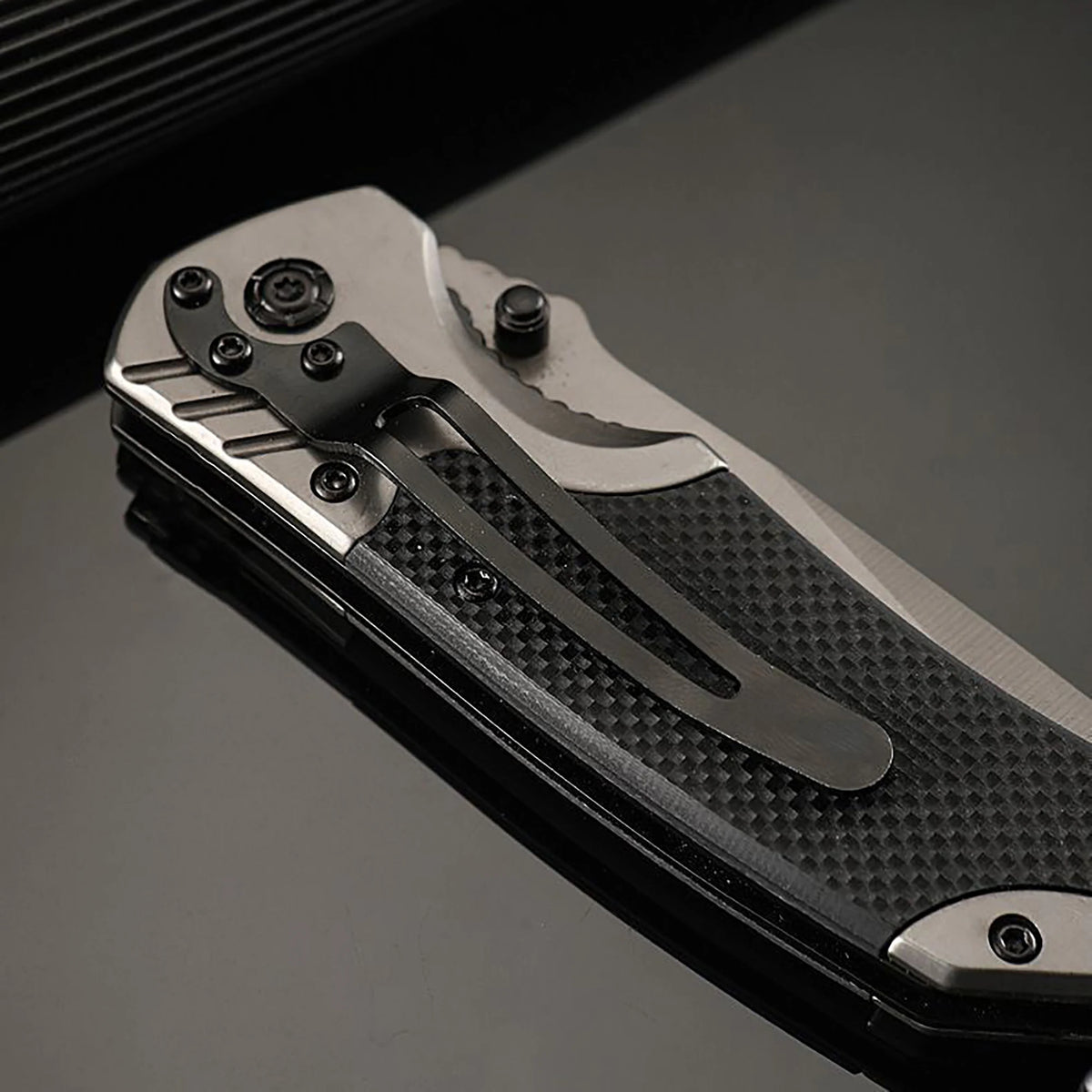 A close-up view of a multi-functional folding survival knife with a textured black handle and silver blade, resting on a dark