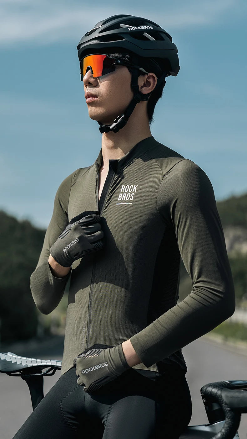 A male cyclist wearing a dark olive performance jersey and black gloves, looking forward while riding a bicycle.