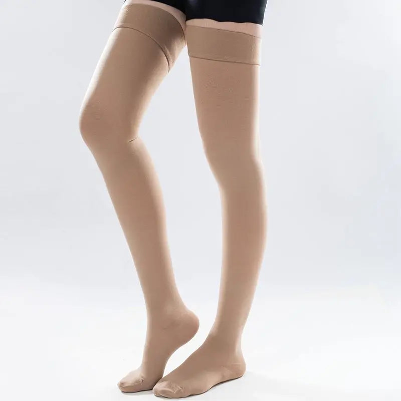 A pair of beige medical compression stockings being worn on a person's legs.