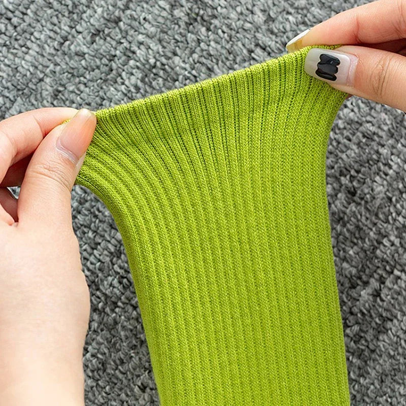 Eine Hand hält einen leuchtend limettengrünen, gerippten Yoga- oder Fitnesssock gegen einen grauen strukturierten Hintergrund