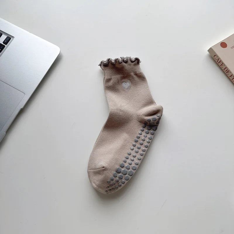 A pair of beige embroidered yoga socks with a textured toe and heel, lying on a white surface.