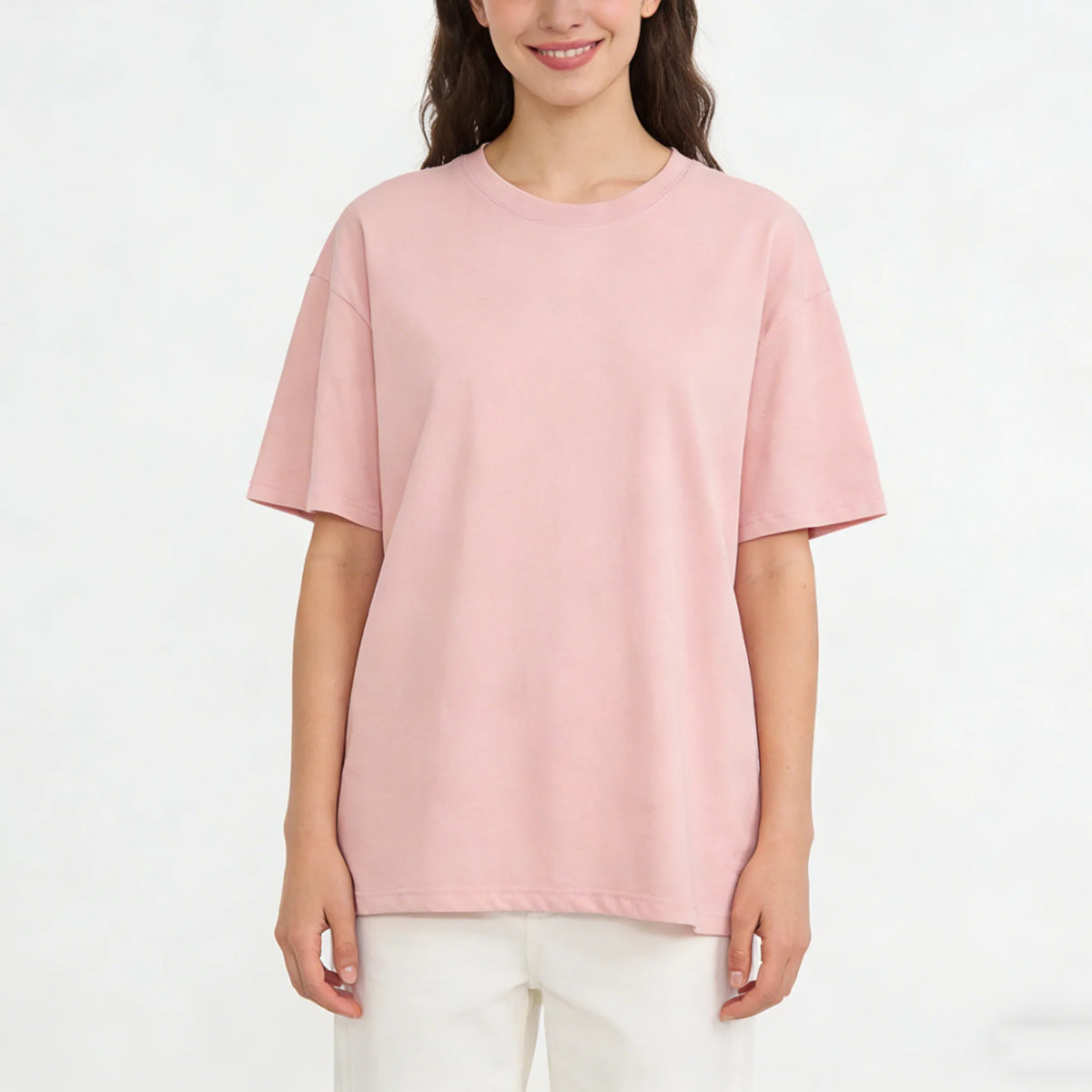 Eine Frau trägt ein hellrosa, oversized Baumwoll-T-Shirt und weiße Hosen.