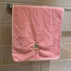 A pink coral fleece face towel hanging on a bathroom rack.