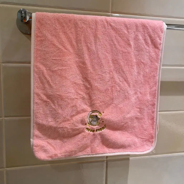 A pink coral fleece face towel hanging on a bathroom rack.