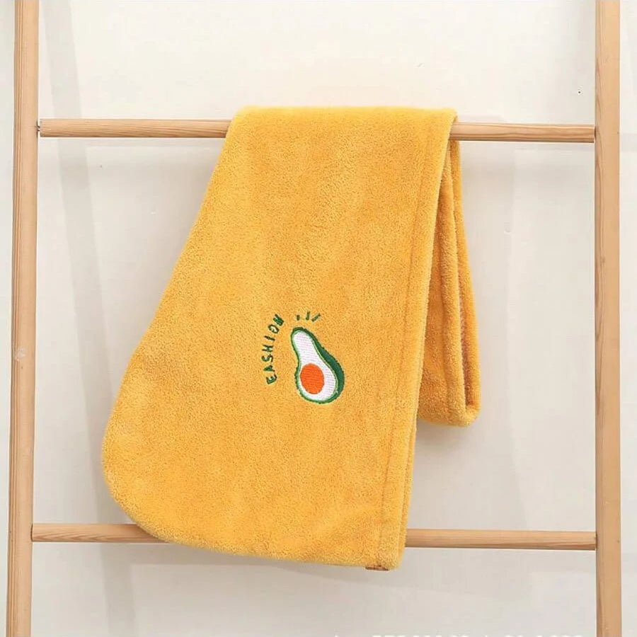 Helles gelbes, flauschiges Haartrockentuch mit grüner Avocado-Stickerei an einem Holzständer.