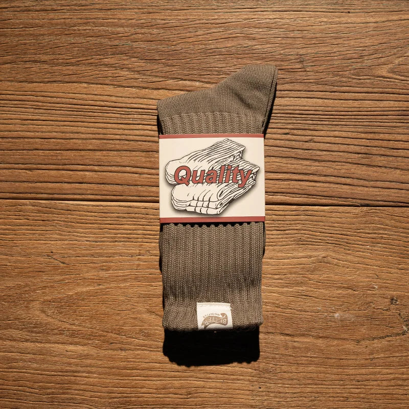 A pair of olive green thick cotton tube socks with a quality label on the cuff, resting on a wooden surface.