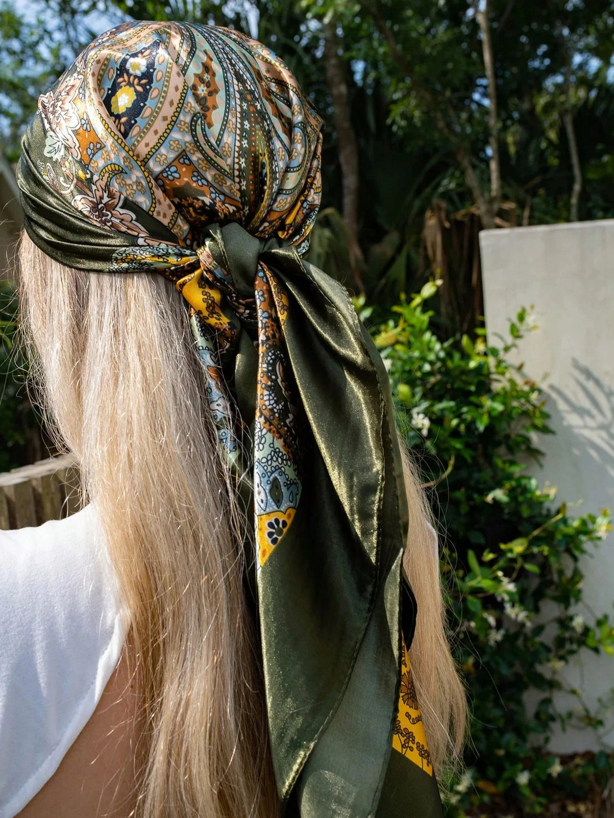 Una mujer con cabello rubio largo lleva una bufanda de satén verde con un intrincado patrón paisley.