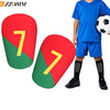 A blue-shirted boy wearing red and green soccer shin guards with the number 7 on them.
