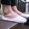 Une paire de chaussettes invisibles en silicone blanches et respirantes portées par une personne, posées sur une surface en b