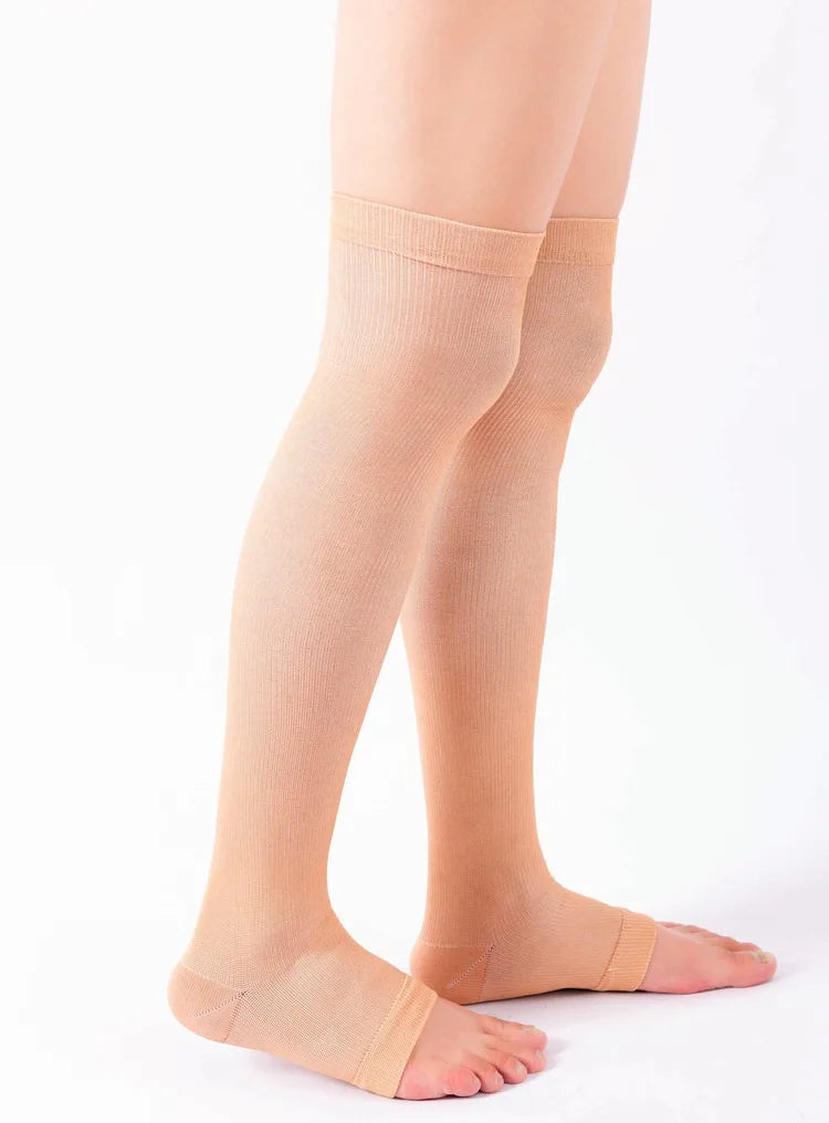A pair of beige compression thigh high socks worn on a person's legs.