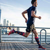 A man wearing high-performance knee-high compression socks is jogging outdoors on a wooden deck.