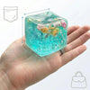 A hand holds a translucent blue fidget cube filled with glitter and small decorative elements.