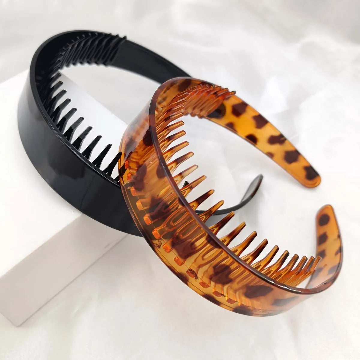 Nahaufnahme eines eleganten Plastik-Haarreif mit Leopardenmuster neben einem schwarzen Haarreif.