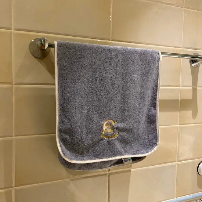 A gray soft coral fleece face towel hanging on a metal rack against a tiled wall.
