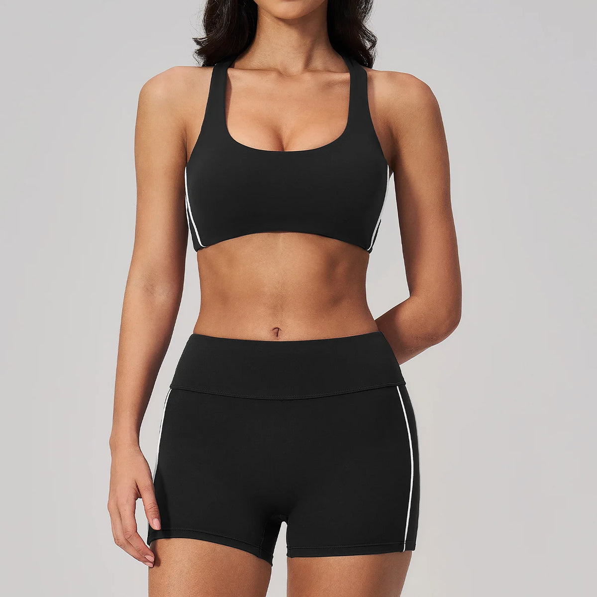 A woman wearing a black two-piece yoga and sports tracksuit set consisting of a sports bra top and matching shorts.