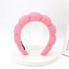 A pink sponge terry cloth headband for hair styling displayed on a white circular stand.