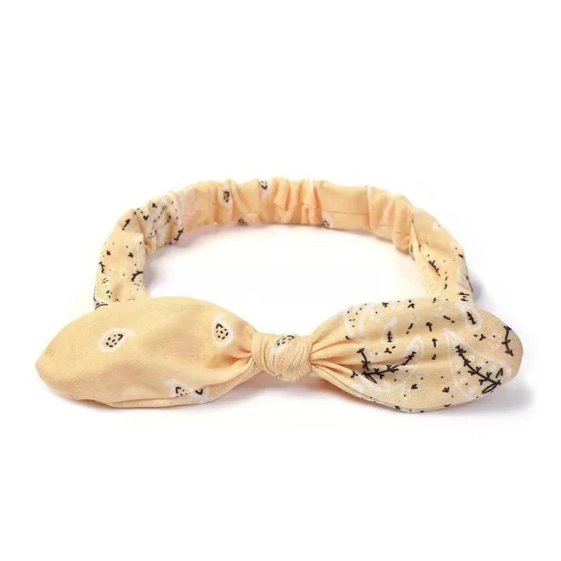 A beige fabric elastic hair headband with a subtle black floral paisley print.