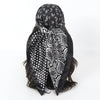 Black satin square scarf with white paisley and polka dot patterns tied around dark hair