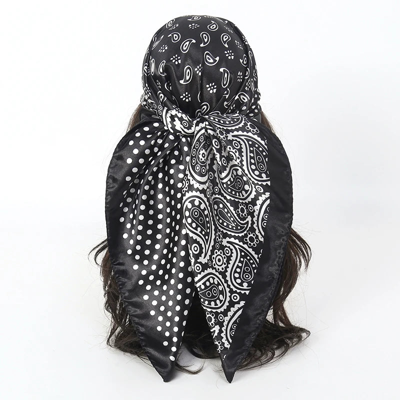 Black satin square scarf with white paisley and polka dot patterns tied around dark hair