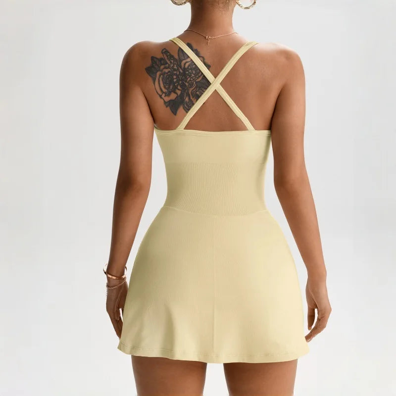 Eine Frau trägt ein hellgelbes Tennis-Skortkleid mit Kreuzriemen und ein Tattoo auf der Schulter.