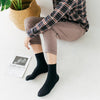 Une personne portant un pantalon marron et une chemise à carreaux est assise, affichant des chaussettes noires à col roulé.
