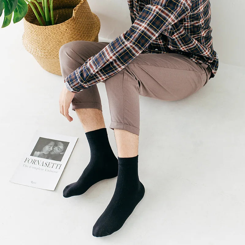 Une personne portant un pantalon marron et une chemise à carreaux est assise, affichant des chaussettes noires à col roulé.