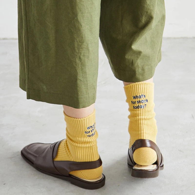 A person is wearing mustard yellow embroidered cotton socks and brown loafers.
