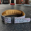 A purple patterned weightlifting belt with a black buckle resting on a dark gray floor.