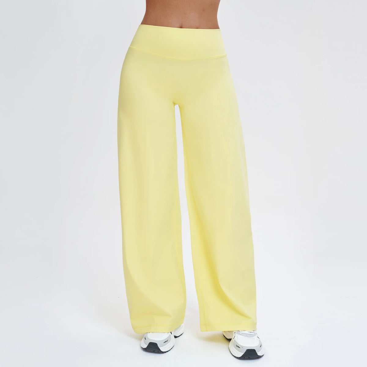 A person wearing light yellow high-waist wide-leg yoga leggings and white athletic shoes.