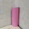A pink hexagonal EVA foam yoga roller standing upright against a light tiled wall.