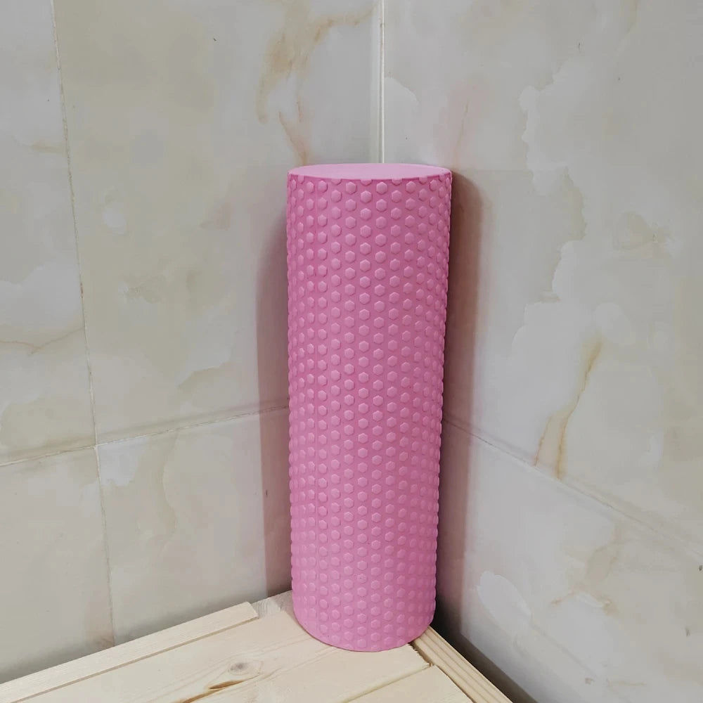 A pink hexagonal EVA foam yoga roller standing upright against a light tiled wall.