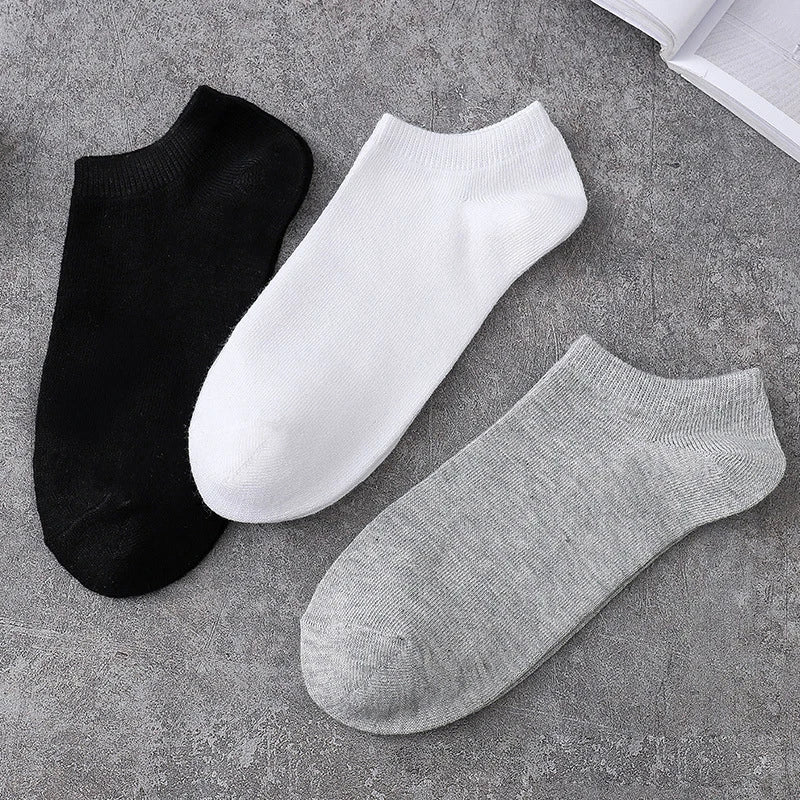 A stack of three ankle socks in black, white, and gray are displayed on a gray textured surface.