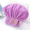 A purple, fluffy hair drying towel cap with a yellow bow is displayed on a white surface.