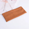 A close-up of a brown ribbed knitted headband lying on a white surface next to some light pink fabric and hands.