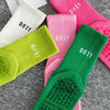 Eine Sammlung atmungsaktiver, rutschfester Yoga- und Fitnesssocken in rosa, weiß und limettengrün auf einer grauen Oberfläche