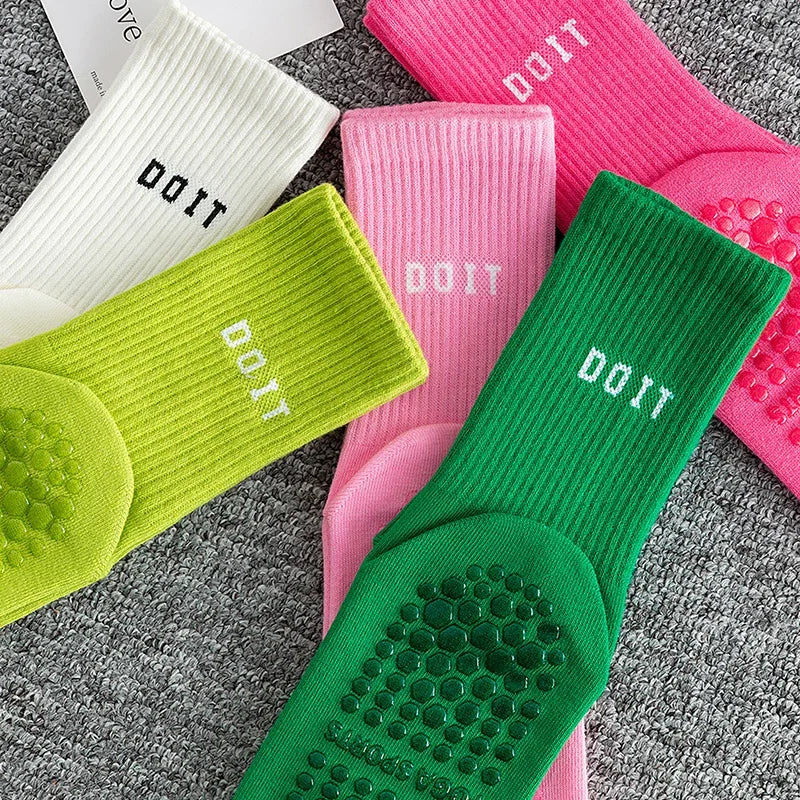 Eine Sammlung atmungsaktiver, rutschfester Yoga- und Fitnesssocken in rosa, weiß und limettengrün auf einer grauen Oberfläche