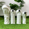 A pair of white golf club head covers resting on green grass with a leafy plant in the background.
