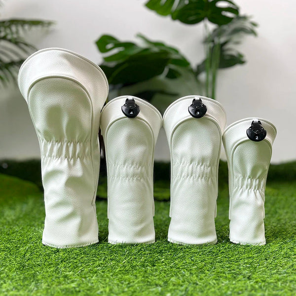 A pair of white golf club head covers resting on green grass with a leafy plant in the background.