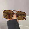 Una mano sostiene unas gafas de sol cuadradas con patrón tortuga y lentes marrones contra un fondo claro.