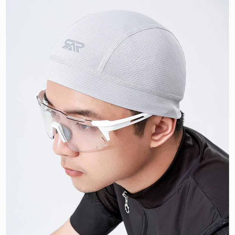 A man wearing a light gray quick dry cycling cap and clear protective eyewear.