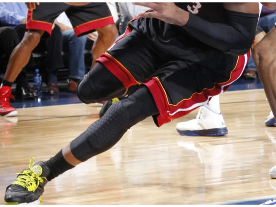 A person wearing black compression knee pads with red trim and black pants is shown during a sports activity.