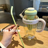A hand holds a clear glass bottle with a green straw and lid, labeled ice cream, on a wooden table.