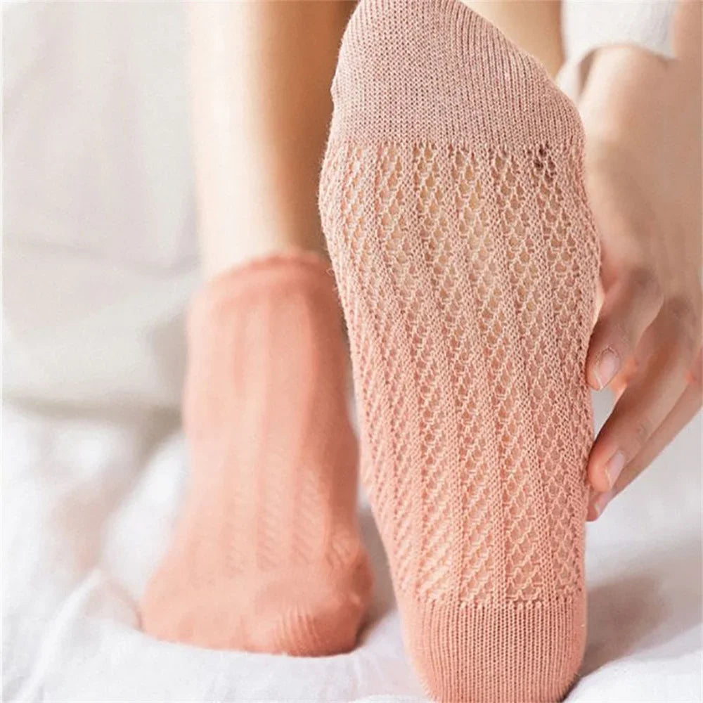 A close-up of a pair of light peach breathable mesh lace tube socks being held by a hand.