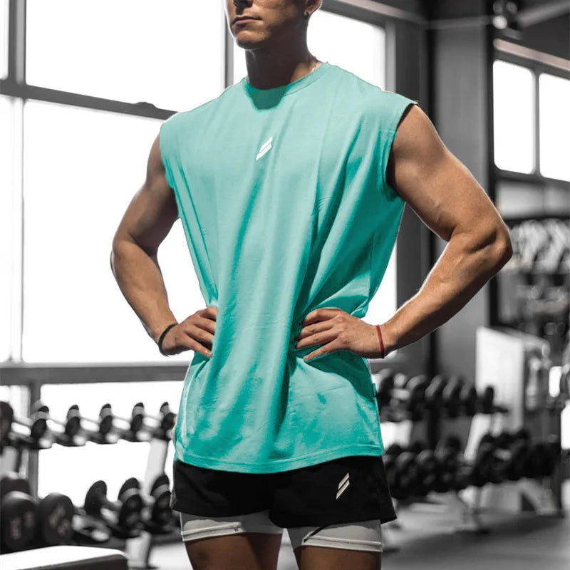 A male model wearing a teal sleeveless fitness tank and black shorts in a gym setting.