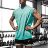 Mann in tealem ärmellosem Fitness-Top und schwarzen Shorts in einem Fitnessstudio.