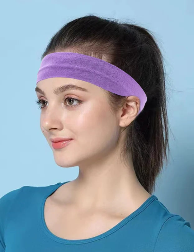 A woman wearing a purple stretchable cotton sweat absorbing headband on her forehead against a light blue background.