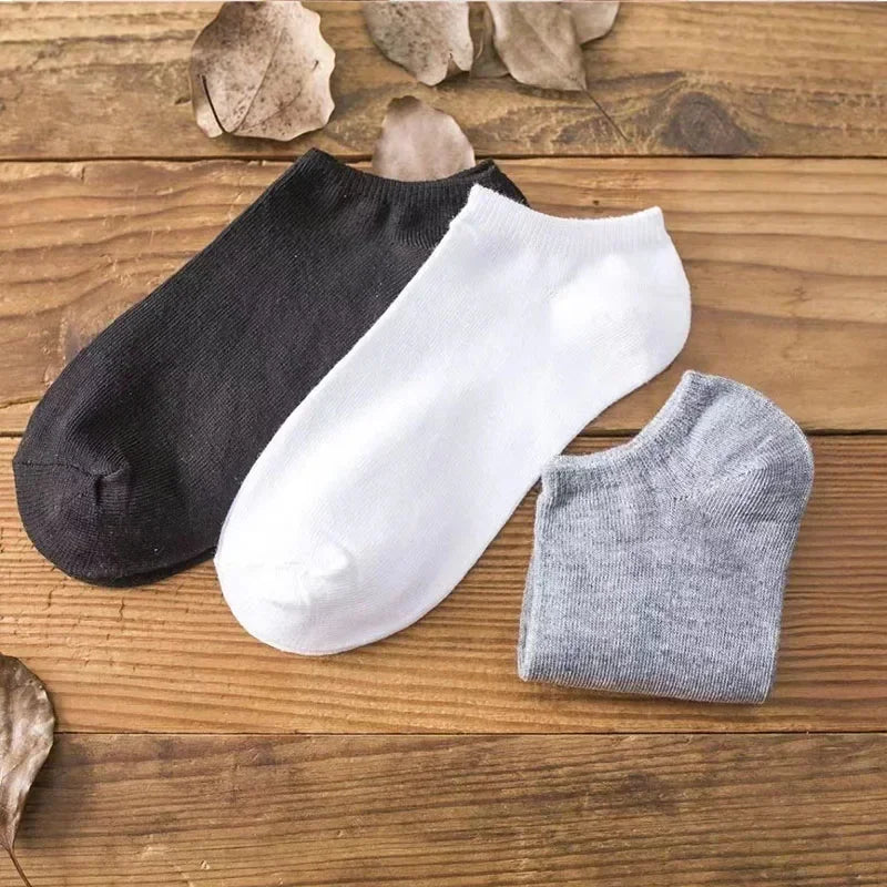 Una exhibición de tres calcetines de tobillo en negro, blanco y gris sobre una superficie de madera.