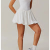 Model trägt ein weißes Performance-Tenniskleid mit gerafftem Rock und grauen Turnschuhen.