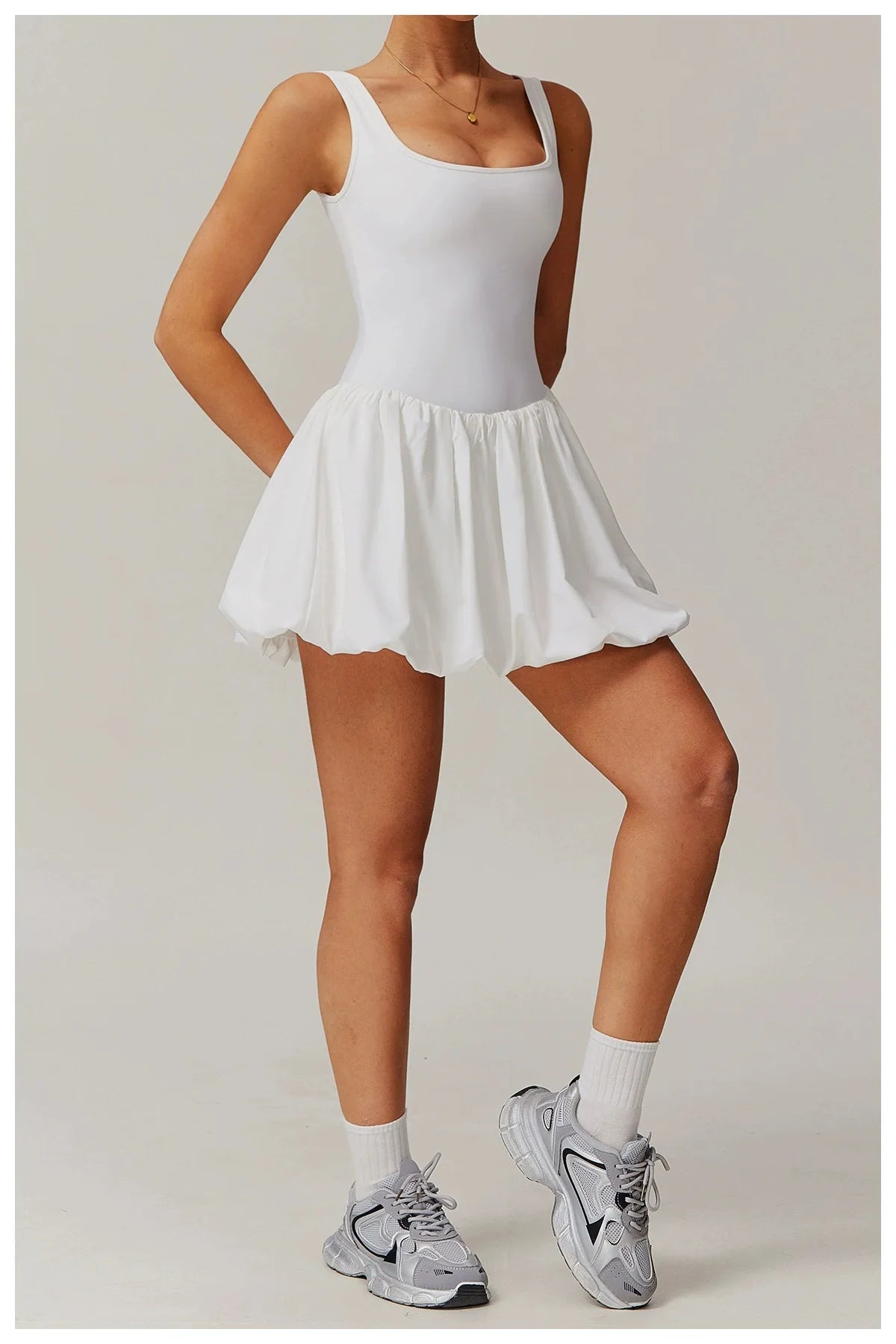 Model trägt ein weißes Performance-Tenniskleid mit gerafftem Rock und grauen Turnschuhen.