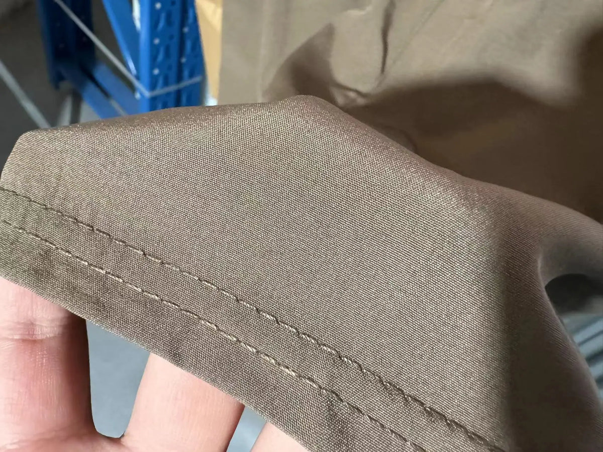 Close-up of a brown men's stretch performance drawstring pant fabric being held by a hand.
